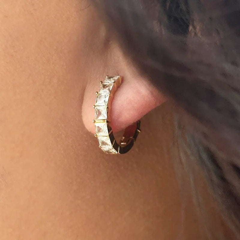 Close-up of gold hoop earring set with square-cut clear gemstones on ear