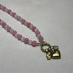 Necklace with pink and white beads and gold heart charm on a light gray background