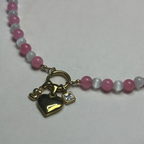 Necklace with pink and white beads and gold heart and square charm on a light background