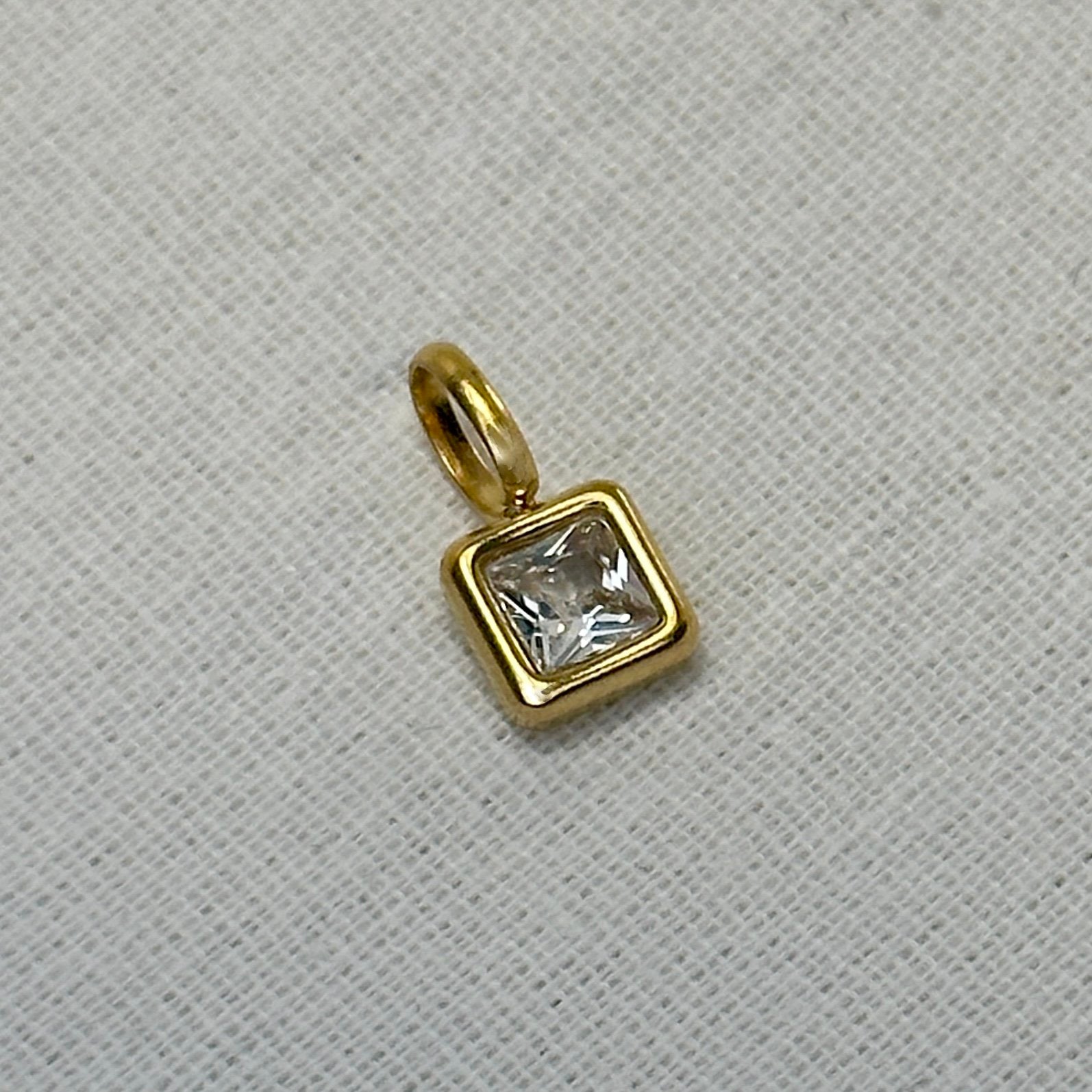 Gold pendant with a clear gemstone on a gray textured background