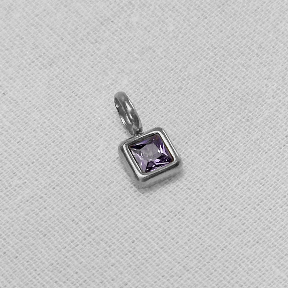 A silver square pendant charm featuring a faceted light purple gemstone, displayed on a textured white fabric background.