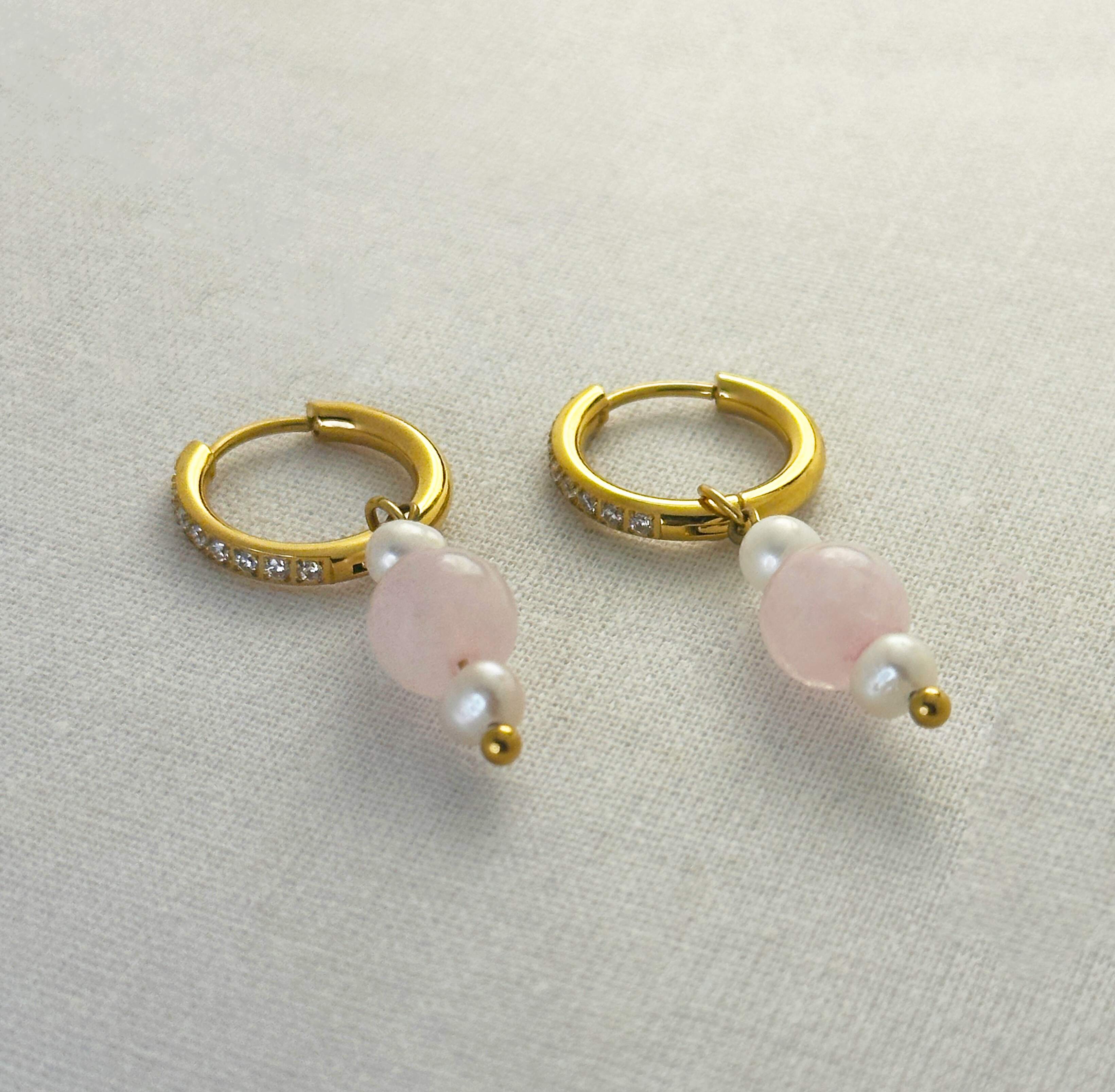 Gold hoop earrings with pink beads on a light gray background