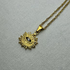 Gold sunburst pendant necklace with central eye and clear gemstone on white fabric