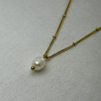 Gold chain necklace with white pearl pendant on light fabric background