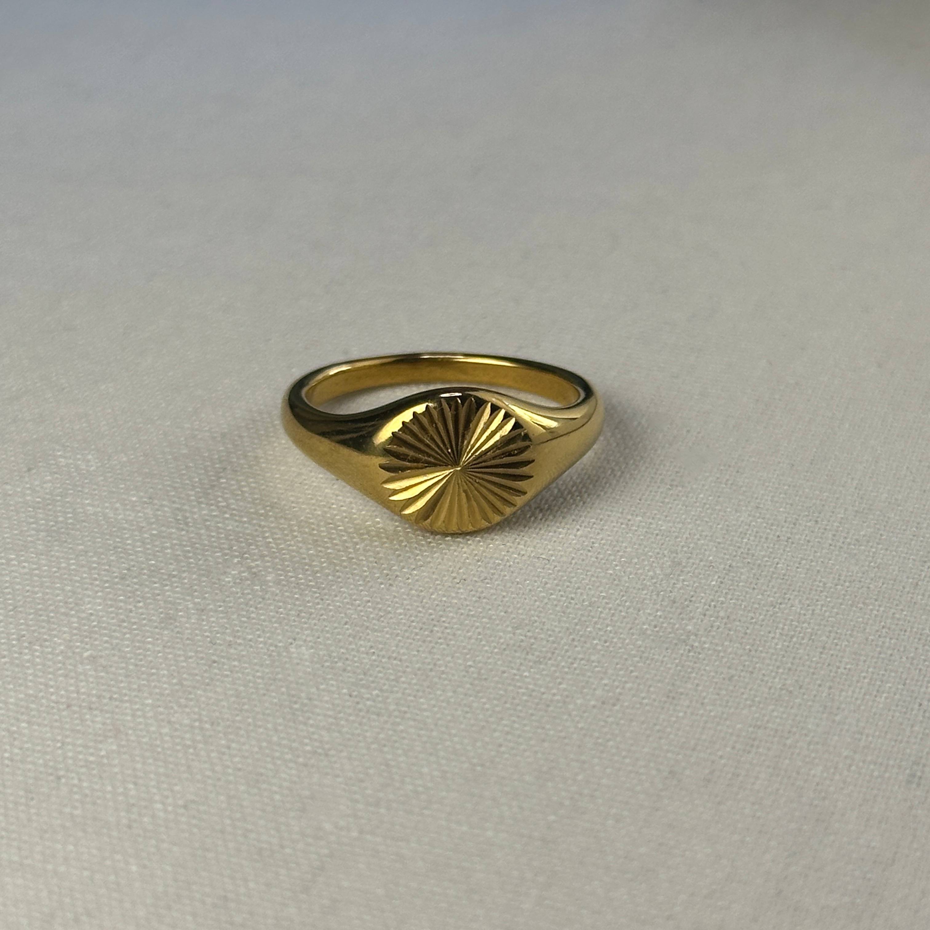 Gold ring with radiating pattern on a white fabric.
