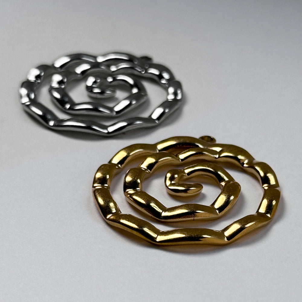 Two metallic spiral-shaped jewelry pieces, one in polished gold and one in polished silver, displayed on a neutral light gray background.