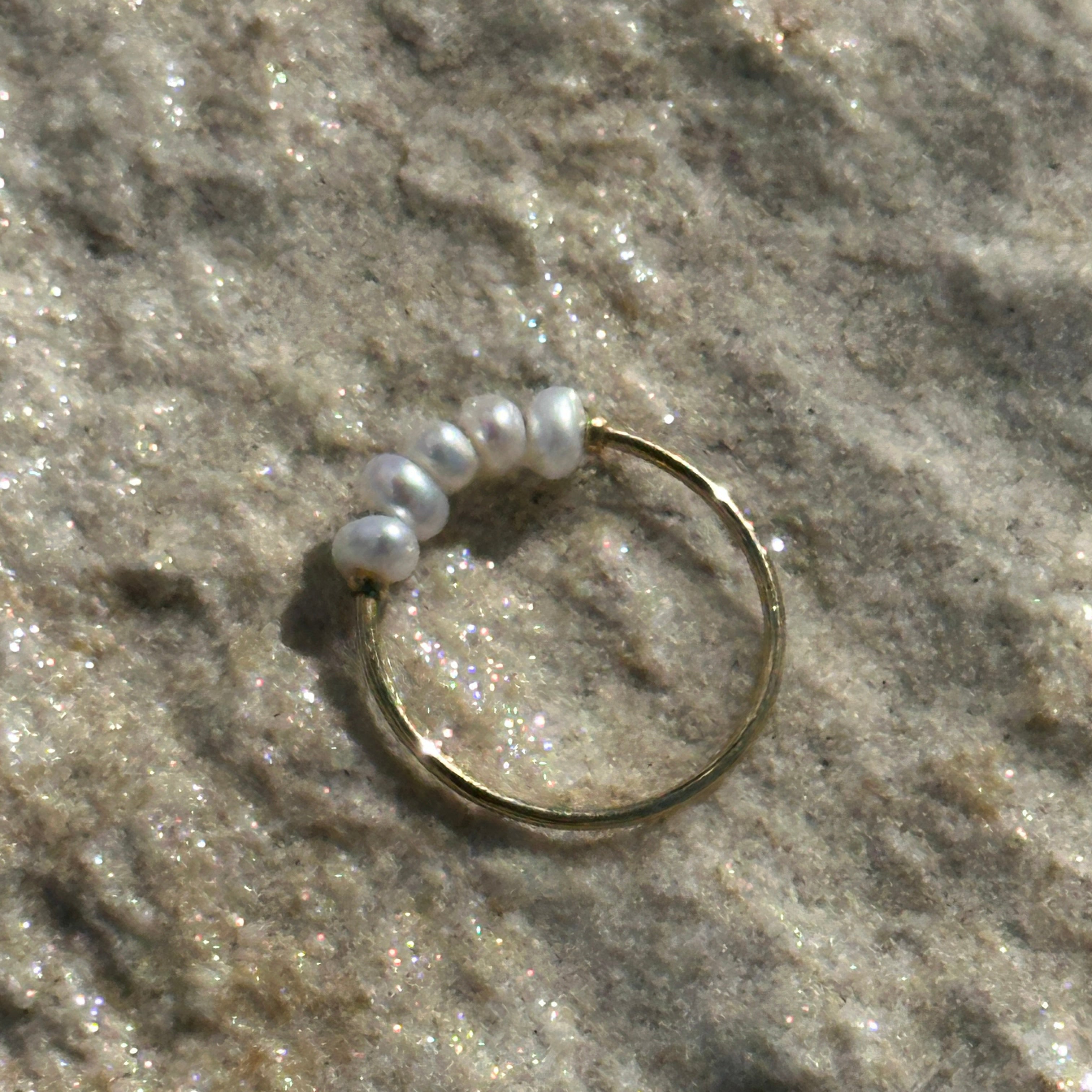 Gold ring with white pearls on a textured surface.