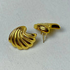 Pair of glossy gold shell-shaped stud earrings on white fabric background