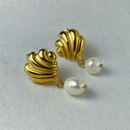 Gold shell-shaped earrings with dangling white pearl accents on light fabric
