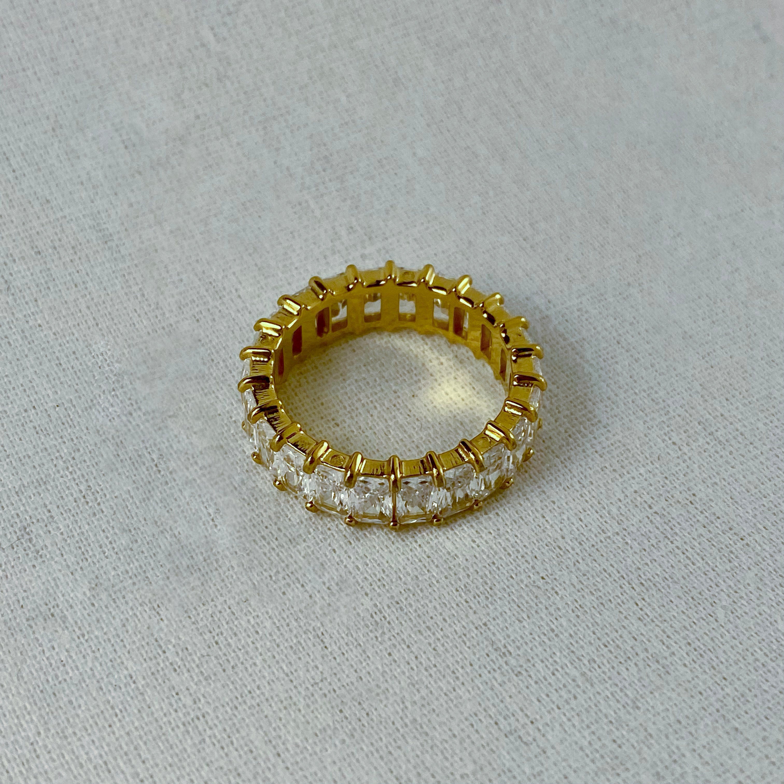 Gold eternity band ring with square-cut crystals.