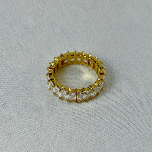 Gold eternity band ring with square-cut crystals.