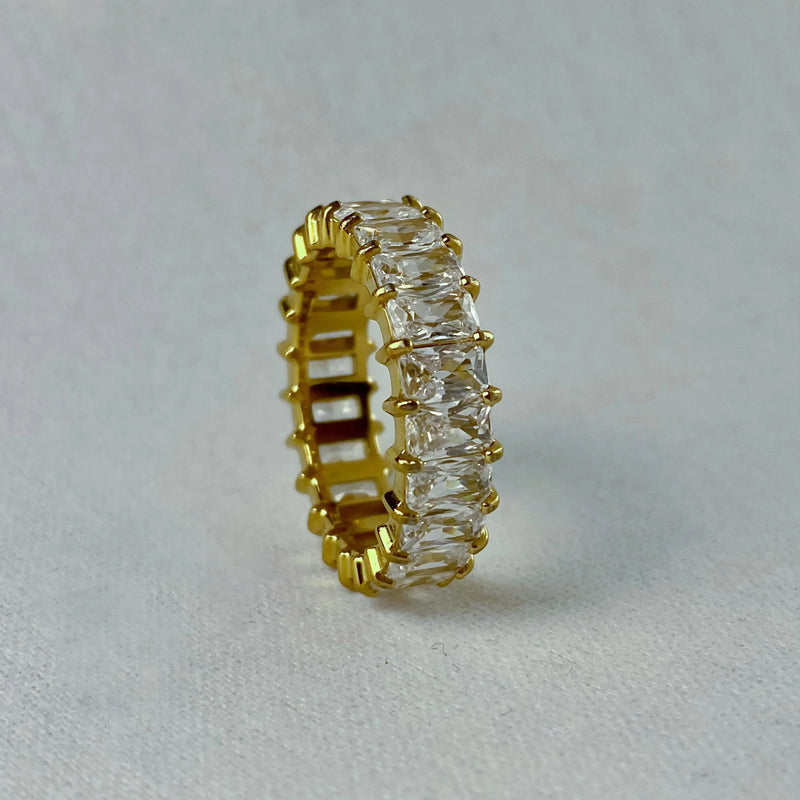 Gold eternity band ring with clear rectangular gemstones on a light grey surface