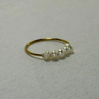 Delicate gold ring with five small white pearls on beige fabric background