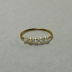 Delicate gold ring with five uneven white pearls on light fabric background