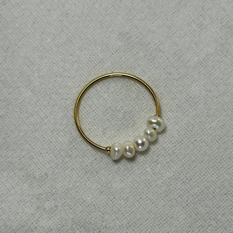 Delicate gold ring with five irregular white pearls on textured beige fabric background