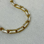 Close-up of gold bracelet with rectangular clear gemstones on beige fabric background