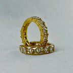 Gold hoop earrings set with square-cut clear gemstones on white fabric background