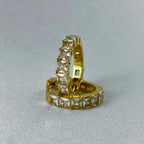 Gold hoop earrings with square-cut clear gemstones on light fabric background