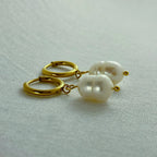 Close-up of gold hoop earrings with white baroque pearl pendants on textured fabric