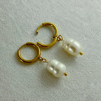 Gold hoop earrings with dangling irregular white pearls on beige fabric background
