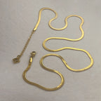 gold snake chain necklace and bracelet set on beige fabric background