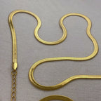 Close-up of a shiny gold herringbone chain necklace on a light fabric background