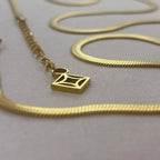 Close-up of gold chain necklace with geometric square pendant on light fabric