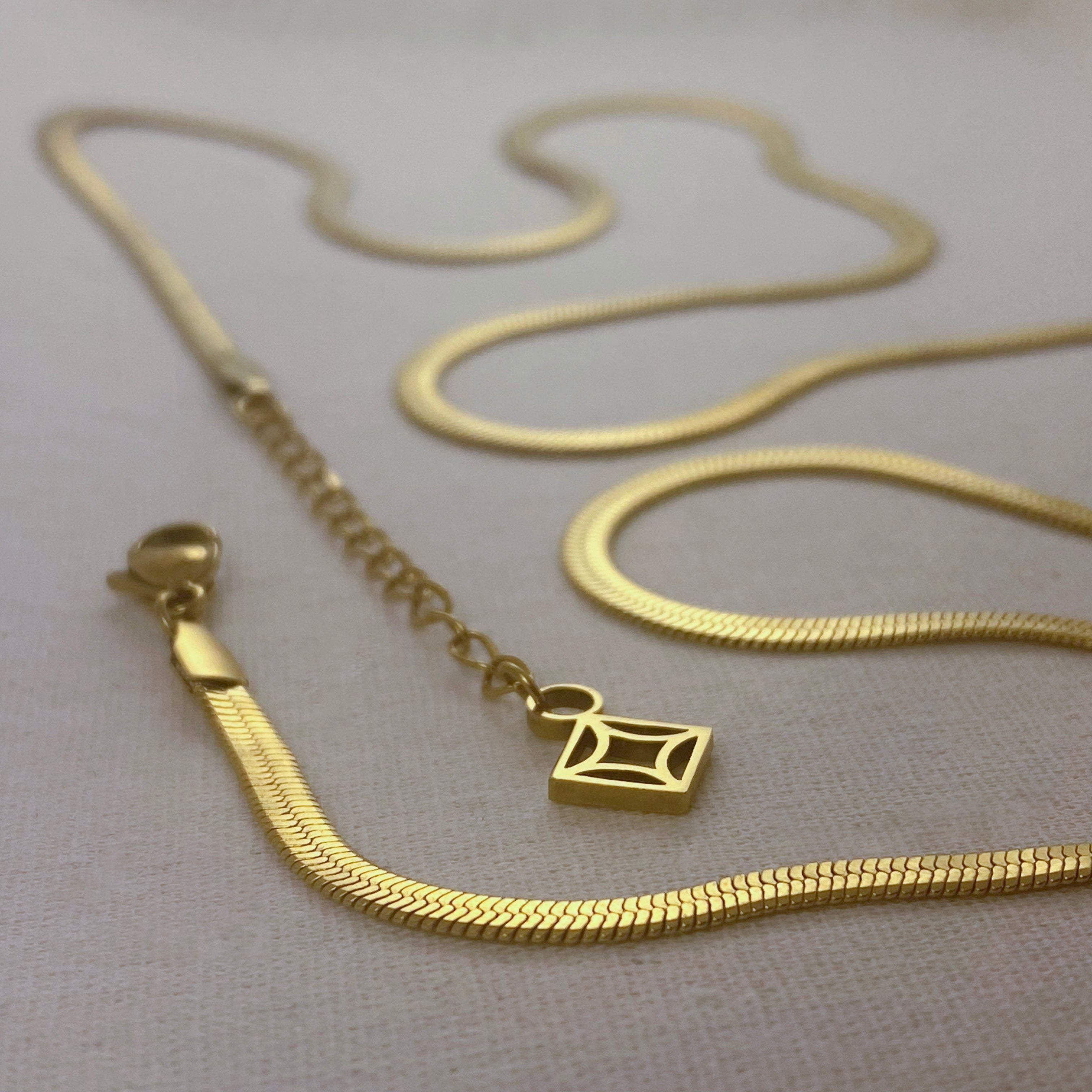 Gold herringbone chain necklace with geometric pendant.