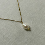 Delicate gold chain necklace with a single white pearl pendant on light fabric background