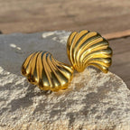 Pair of shiny gold shell-shaped earrings placed on textured beige stone surface
