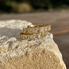 Close-up of two gold rings with square-cut clear gemstones on a textured stone surface