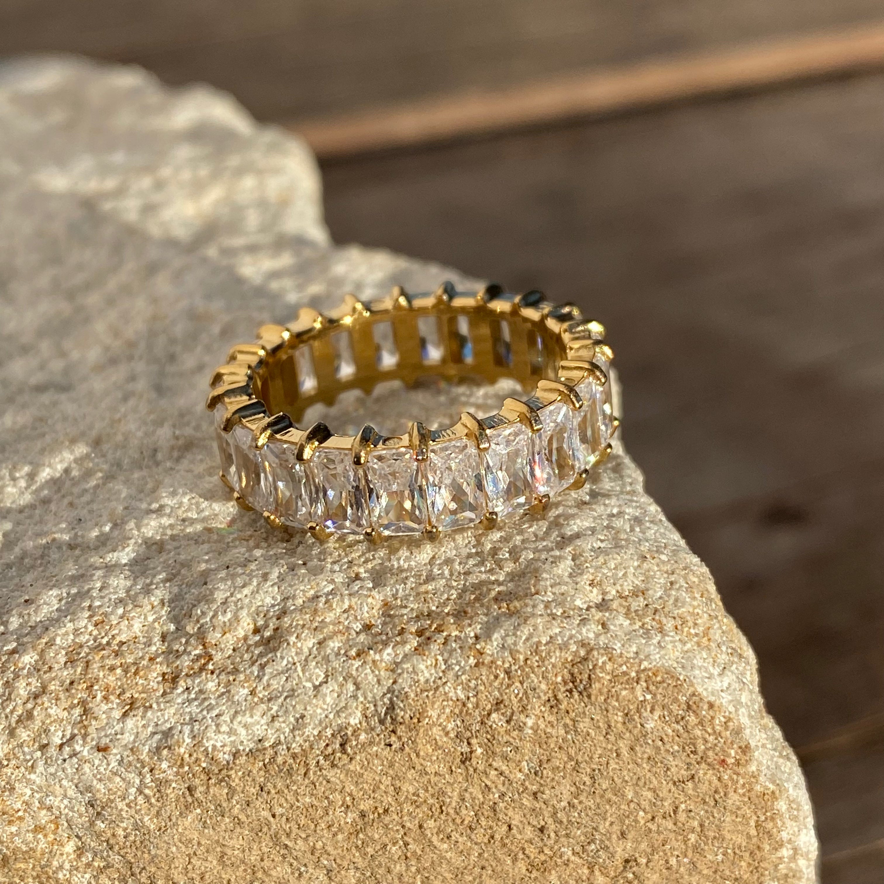Gold eternity ring with rectangular clear stones resting on a textured rock.