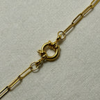 Close-up of a gold chain necklace with a round spring clasp on white fabric background