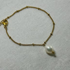 Delicate gold chain bracelet with small beads and a single white pearl pendant on fabric
