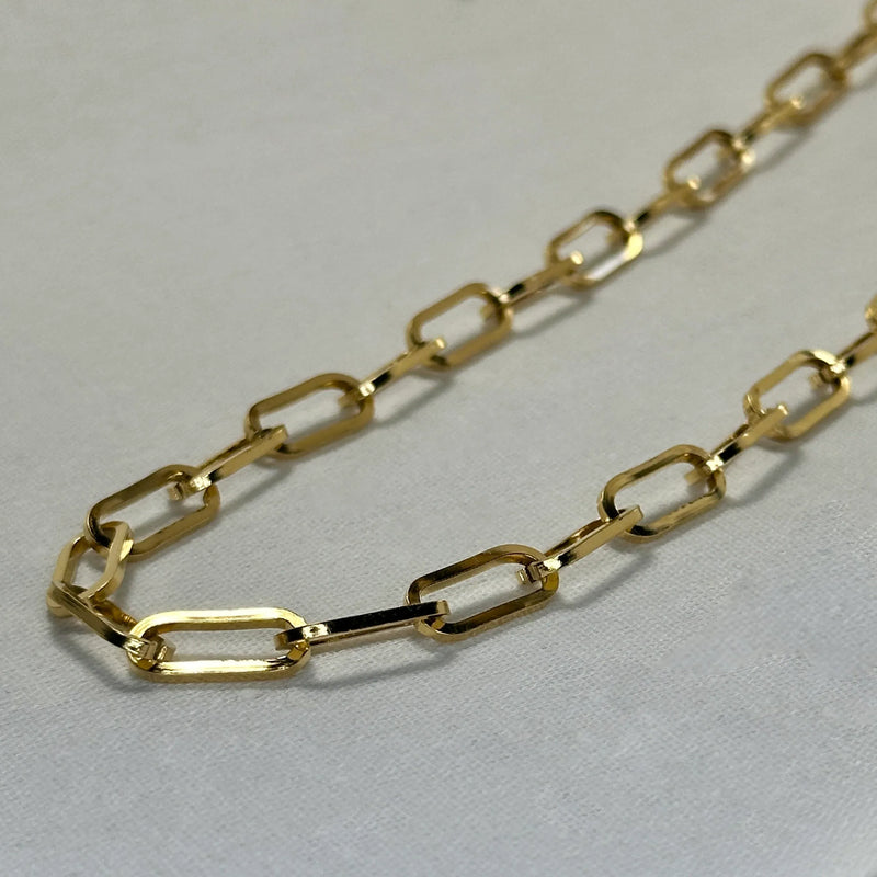 Close-up of a delicate gold link chain necklace on a light fabric background
