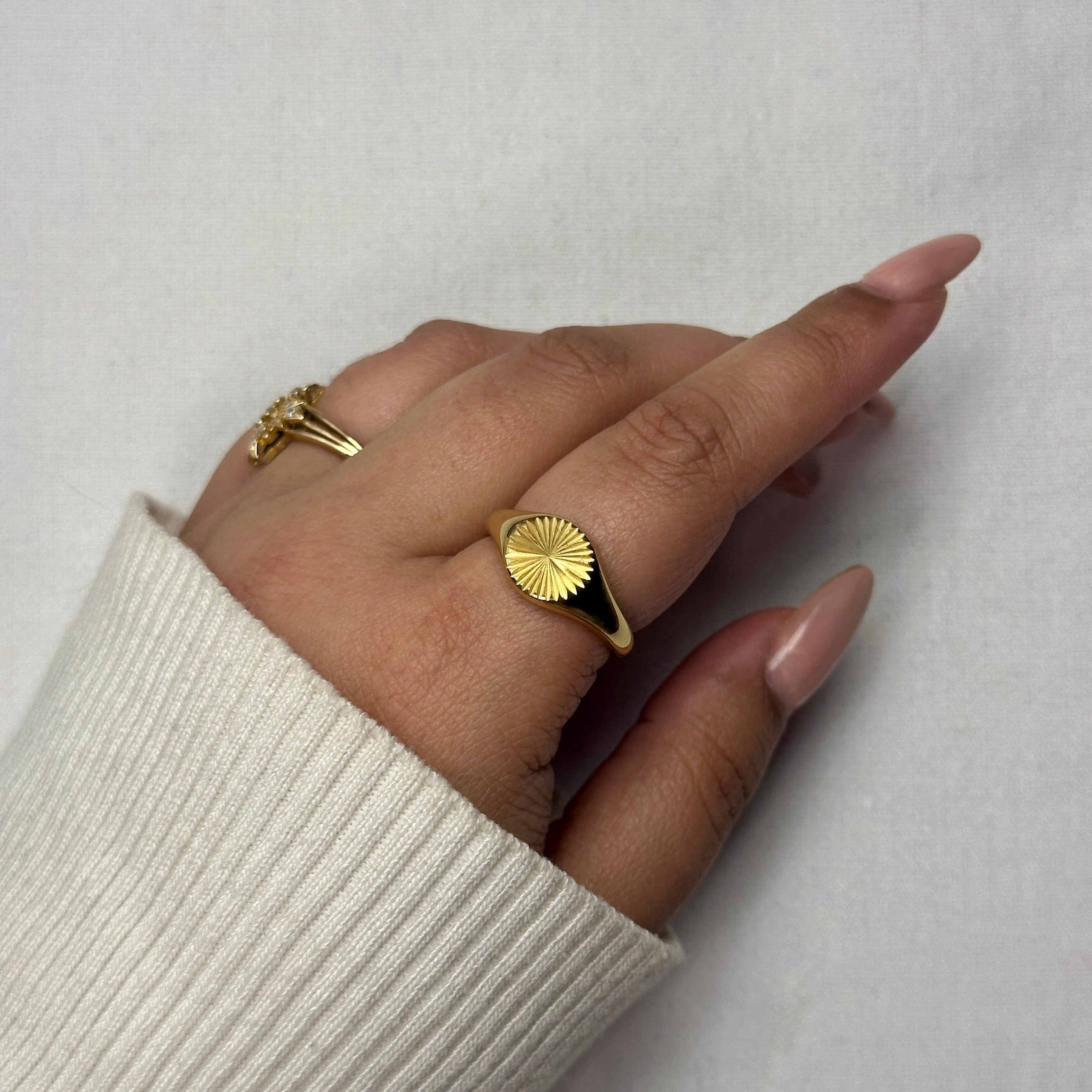 Hand wearing gold signet ring and gold ring with stones, white sweater, nude nails.

