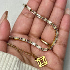 Close-up of hand holding gold bracelet with rectangular clear stones and geometric charm