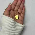 Hand holding gold pendant necklace with engraved flower design on gray background