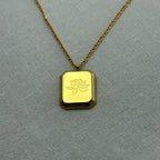 Gold pendant necklace with rectangular floral engraving on textured gray surface
