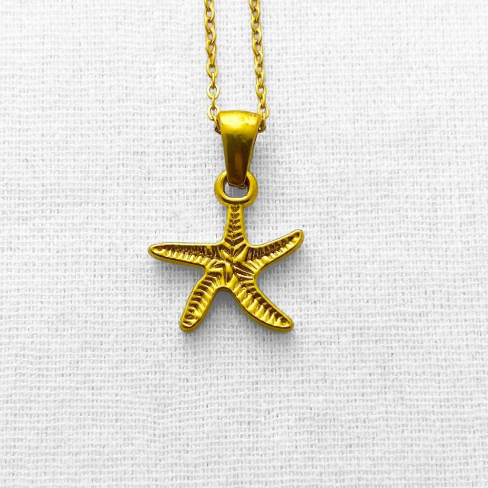 Gold starfish pendant on a chain against a beige background