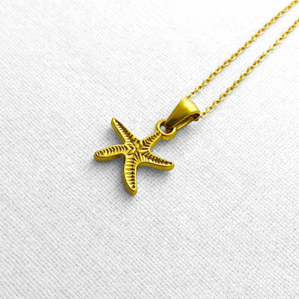Gold starfish pendant on a chain against a beige background