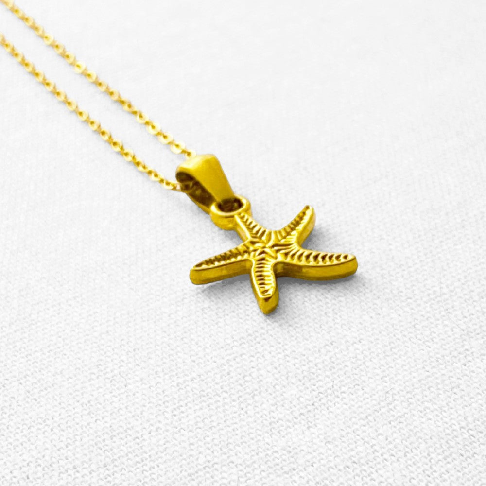 Gold starfish pendant on a gold chain against a beige background
