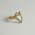 A gold open heart-shaped ring with a textured, hammered finish on a light gray background.