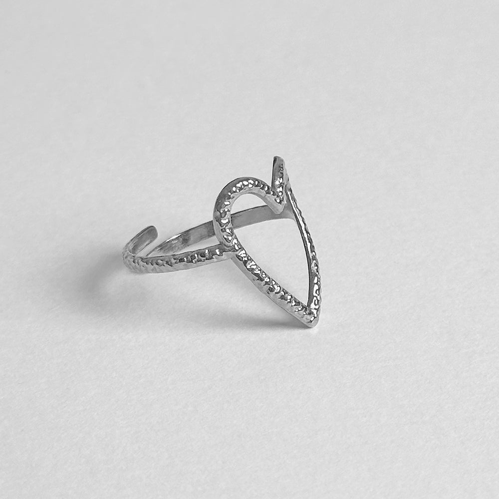 A silver open heart ring with a textured band, photographed on a clean, light gray background.