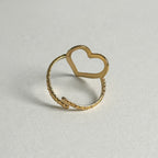 A gold-toned open heart ring with a textured band, photographed on a neutral light gray background.