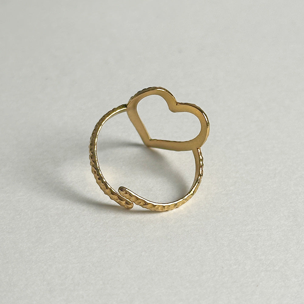 A gold-toned open heart ring with a textured band, photographed on a neutral light gray background.