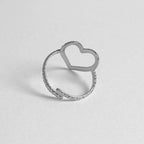 A silver-toned open heart ring with a textured band, photographed on a light gray background.