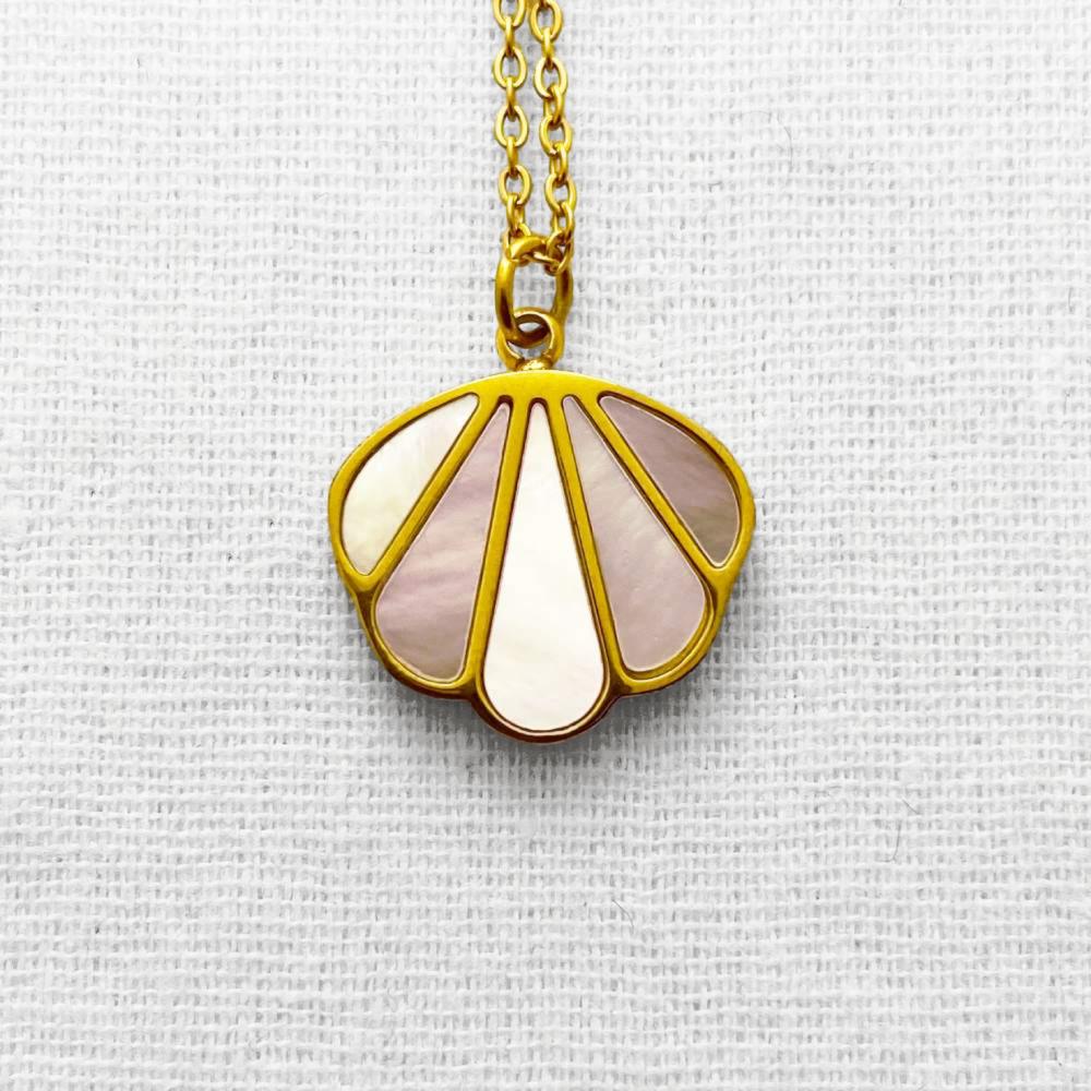 Gold necklace with a shell-shaped pendant on a textured beige background