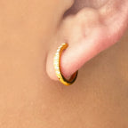 Gold hoop earring worn on a person's ear with a beige background