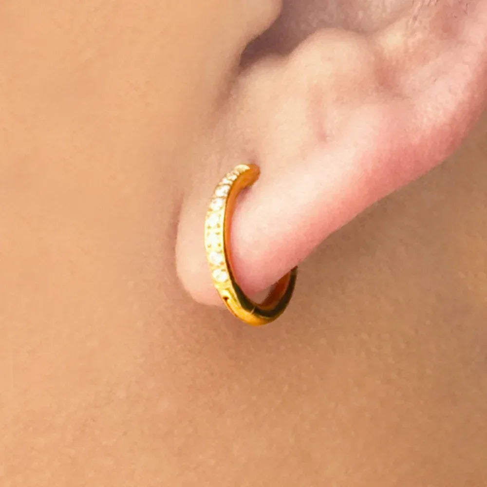 Gold hoop earring worn on a person's ear with a beige background